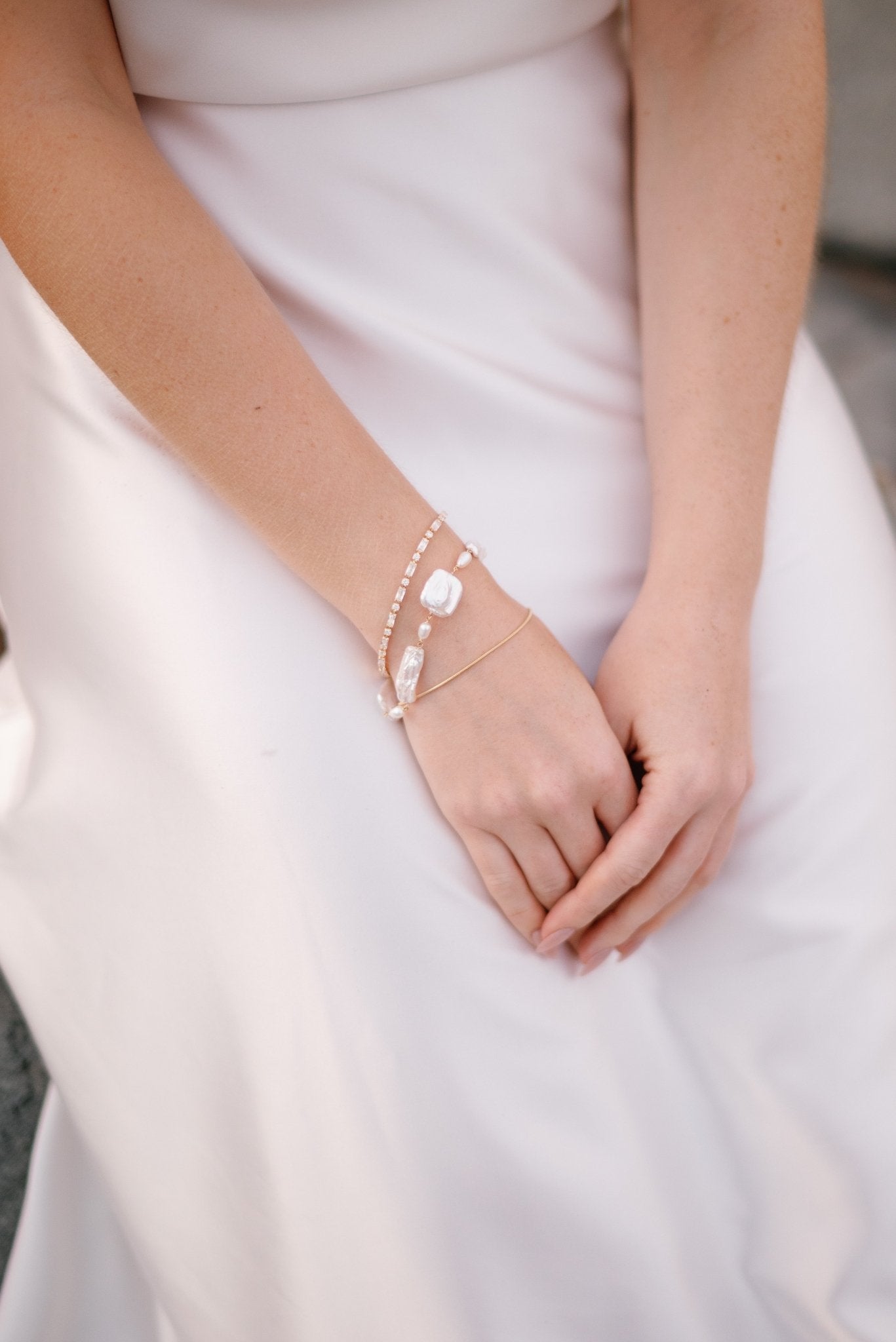 A bride waits patiently while stacked with elegant crystal, pearl, and plain bracelets. 