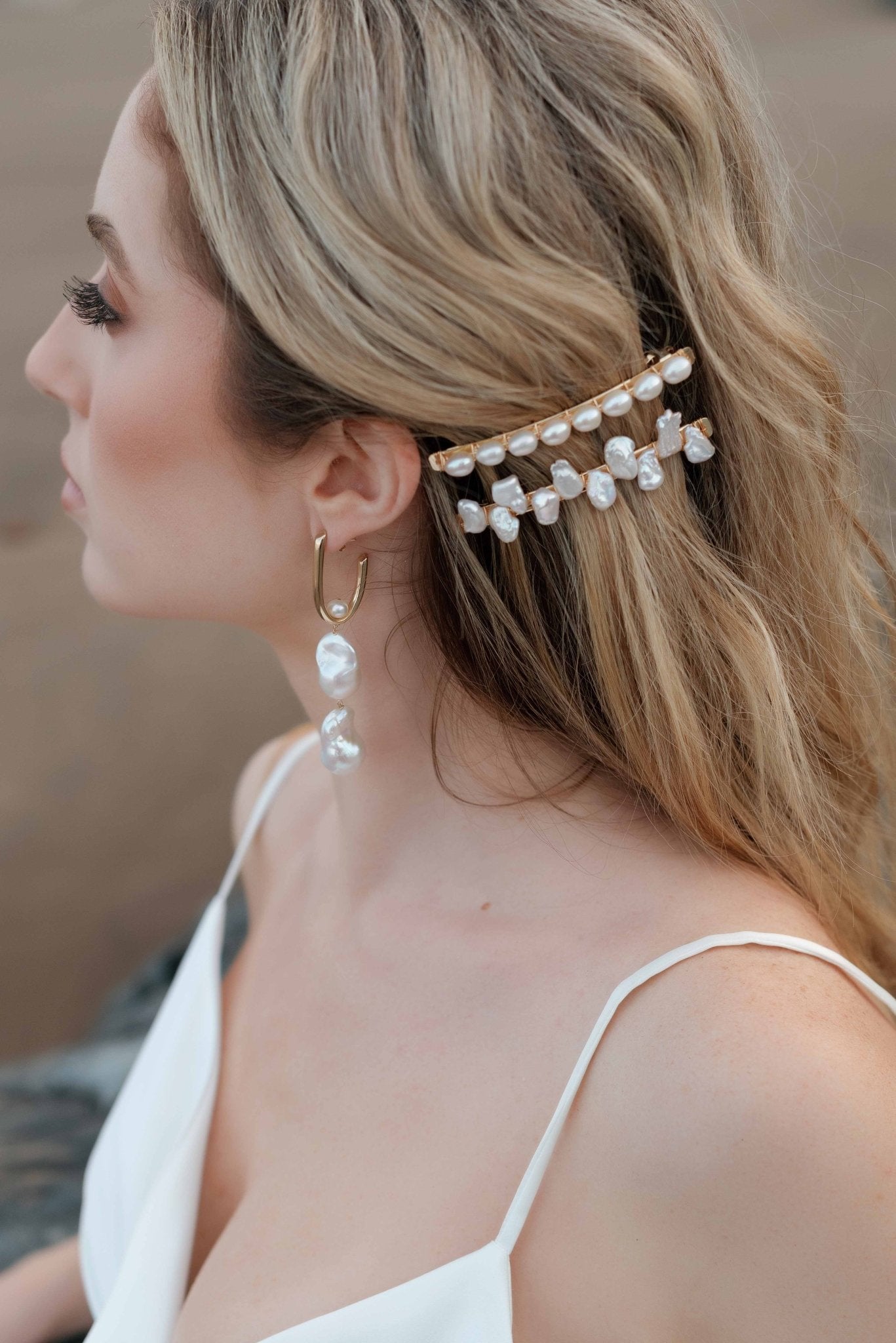 Elegant bride at the beach keeps hair aside with gold and pearl wedding barrettes. She also displays a double baroque pearl hanging earring. 