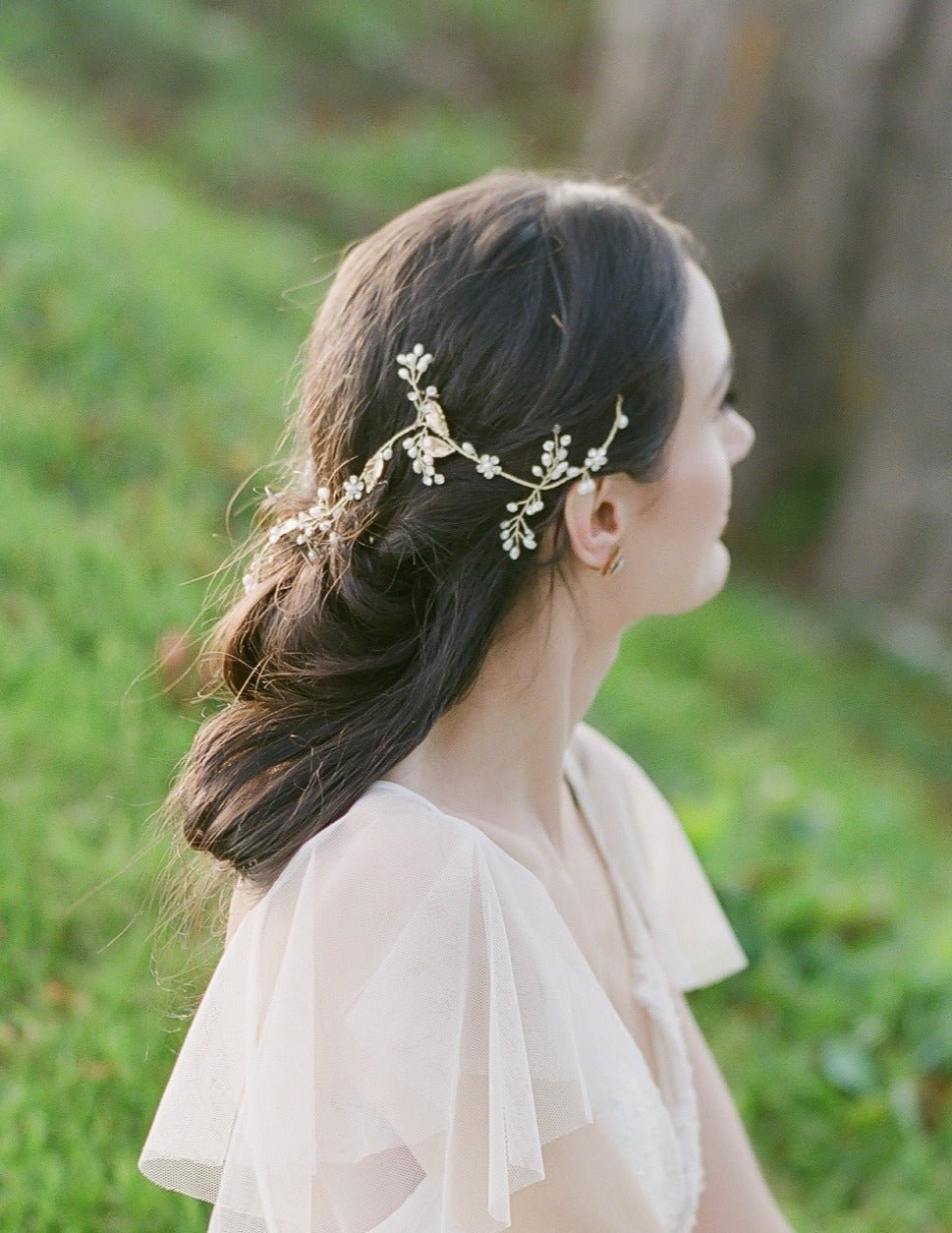 A bride looks out of frame to showcase her looks partial up-do graced with a golden bridal hairvine with freshwater pearls and crystals. 