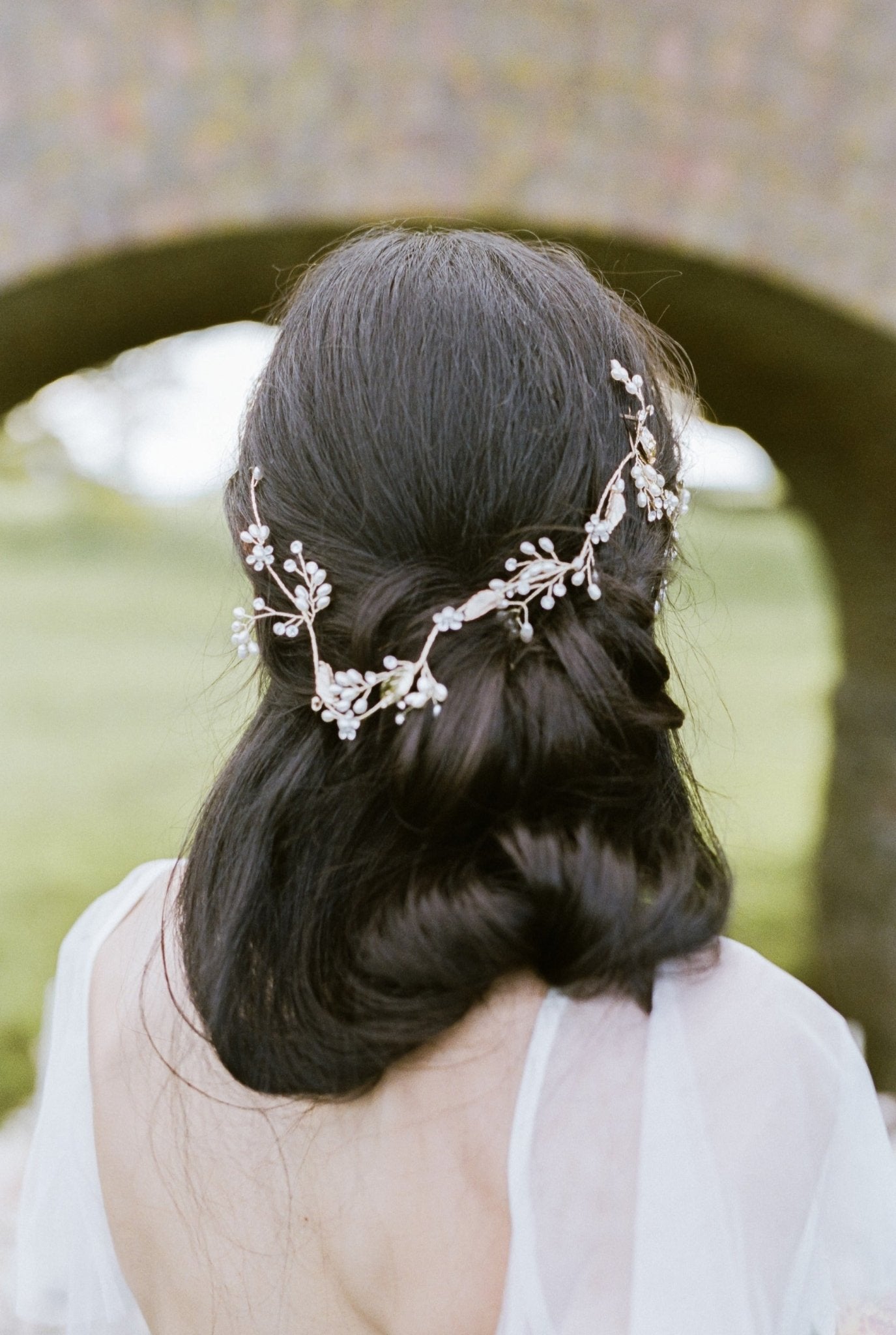 The back view of a bride looking under a bridge to showcase her looks partial up-do graced with a golden bridal hairvine with freshwater pearls and dainty crystals. 