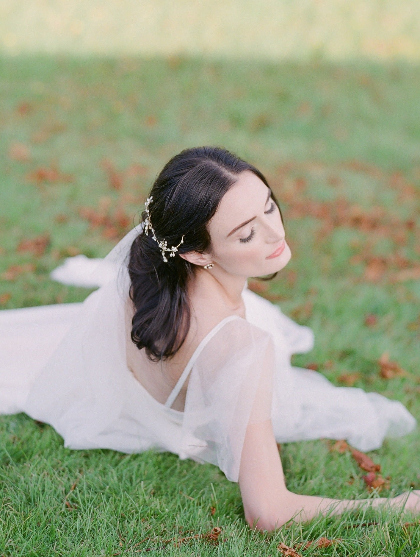 A bride lounges on the grass in a white wedding dress; wistful and ethereal with her bridal hairvine.