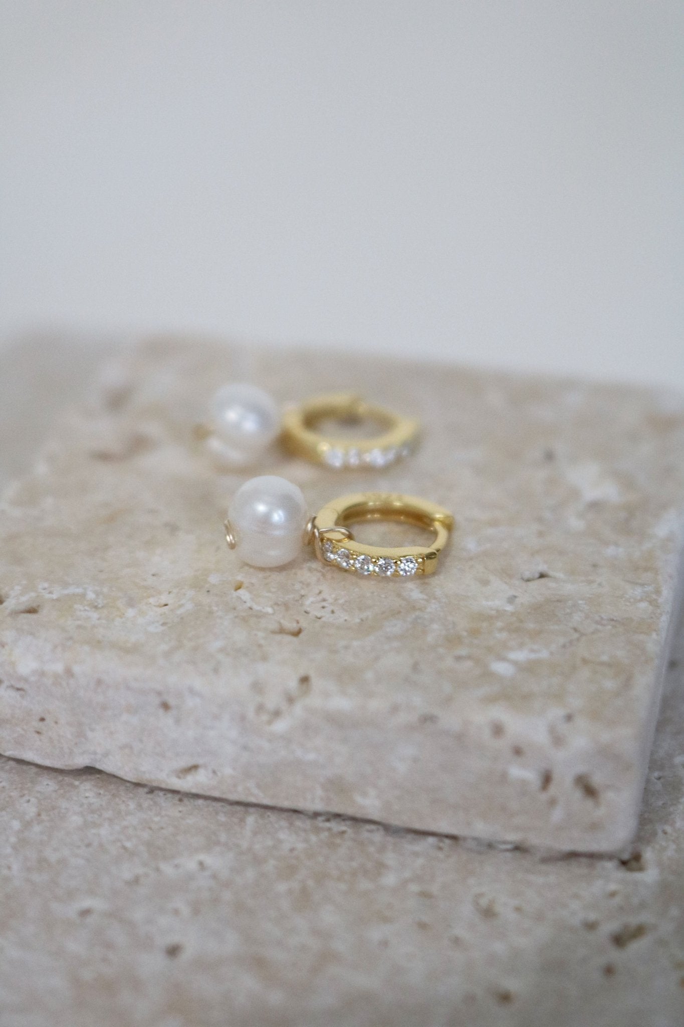 Bridal gold-filled huggies with freshwater pearl drops and cubic zirconia displayed on a stone slab. 