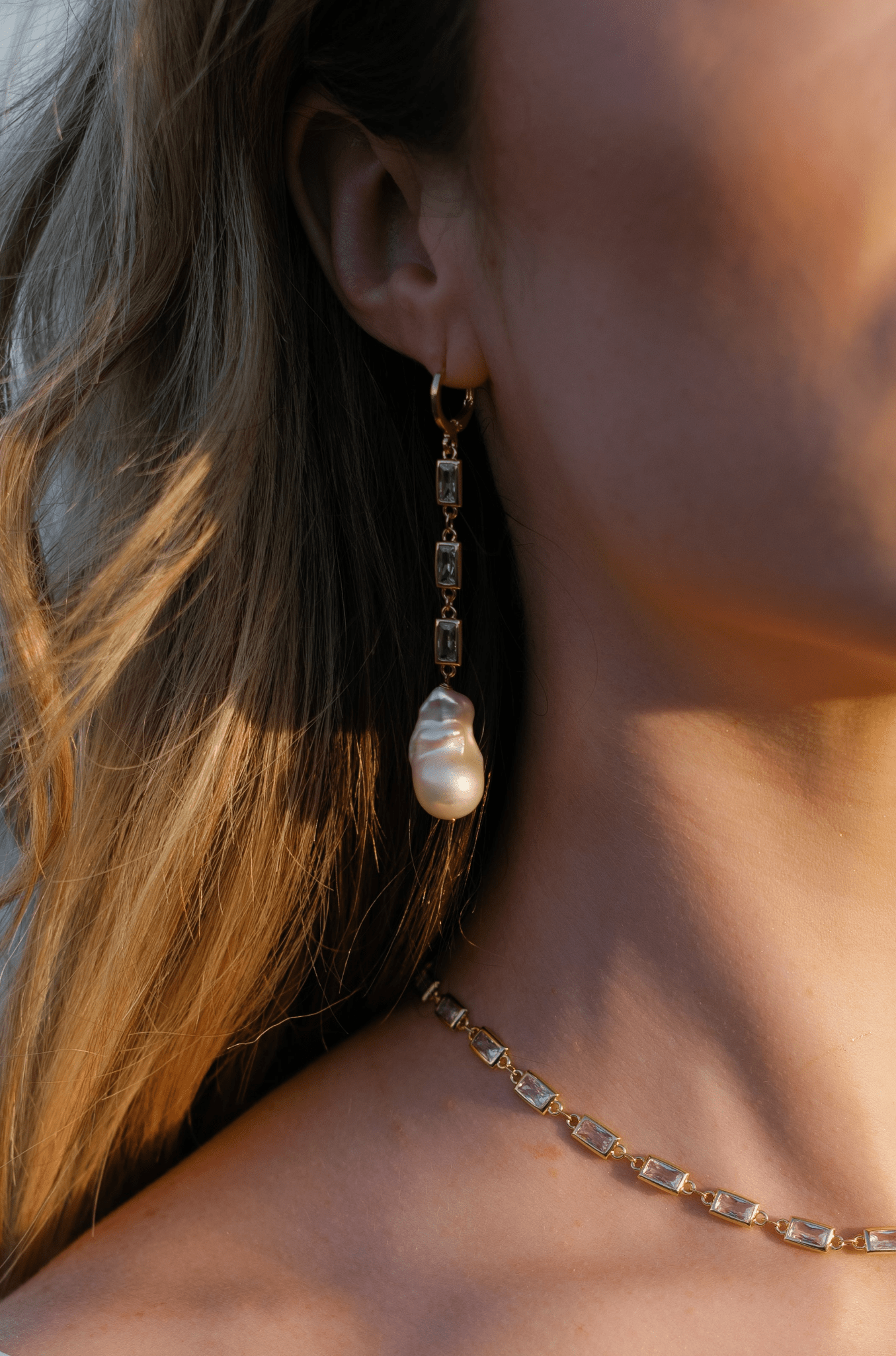 A bride wearing a gold-filled crystal baroque freshwater pearl dangle earring and matching necklace.