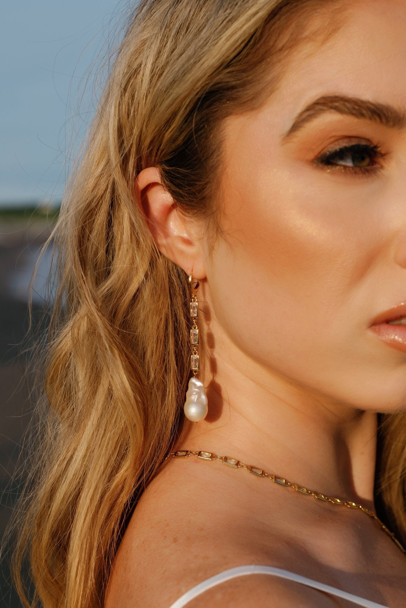 A bride looks away while wearing a gold-filled crystal baroque freshwater pearl dangle earring and matching necklace.