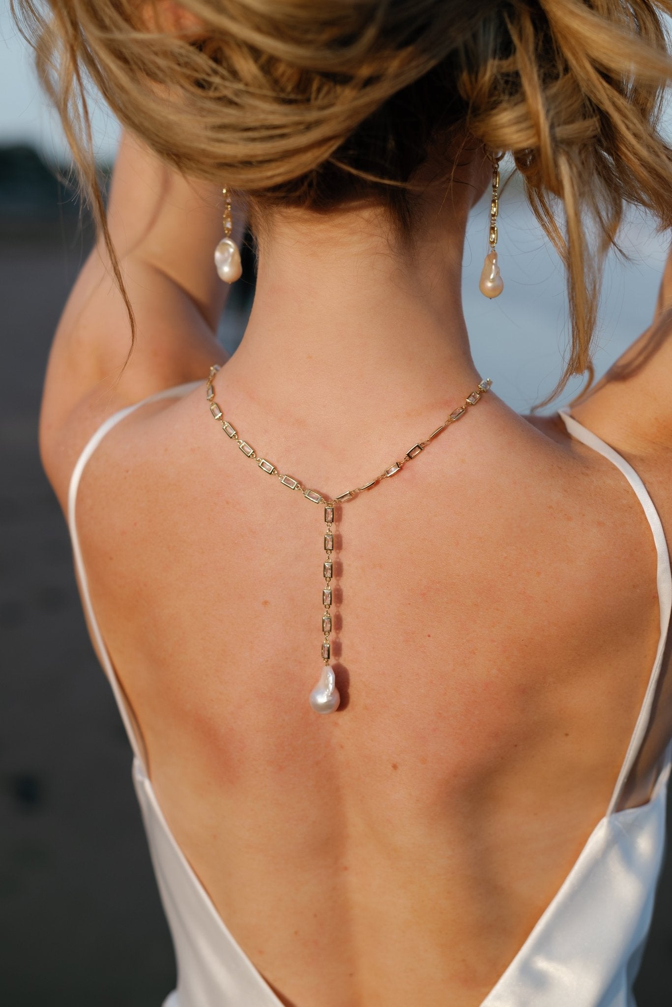 A bride holds her hair up to display her Muse gold-filled crystal Baroque freshwater pearl dangle earrings paired with a gold-filled crystal Baroque freshwater pearl drop necklace draping down her back.