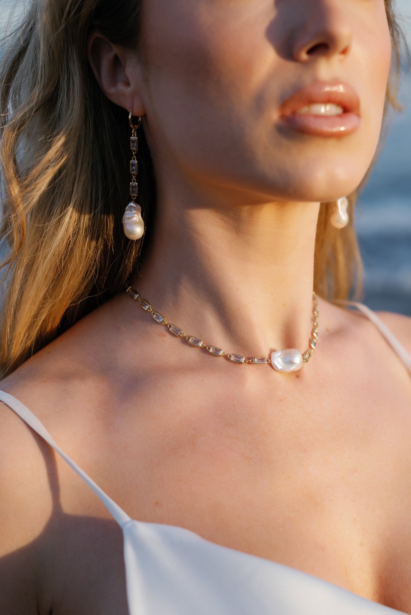 A bride wearing a gold-filled crystal baroque freshwater pearl dangle earring and matching necklace.