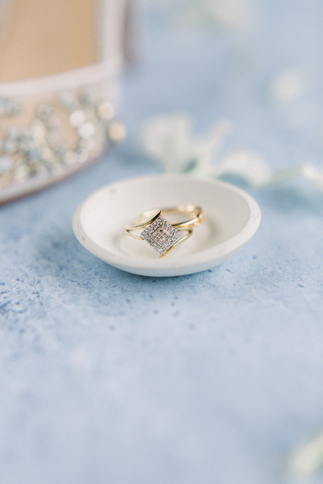 A 10k Yellow & White Gold Vintage Engagement Ring with diamonds sitting in a jewelry dish with blurred background.