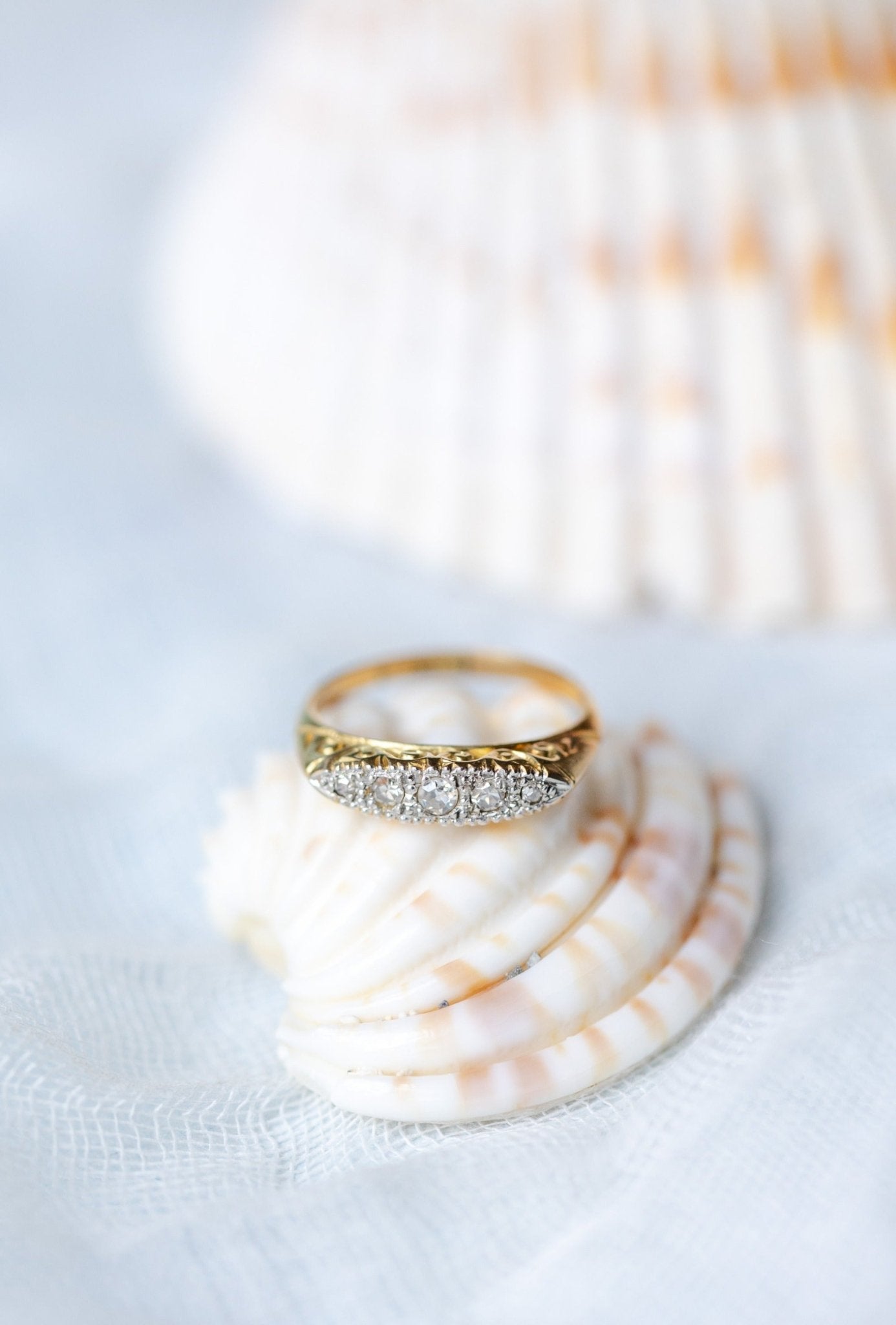 The Odette Art Nouveau 1900s Platinum and 18K Yellow Gold Diamond Vintage Engagement Ring sitting on top of a seashell. 