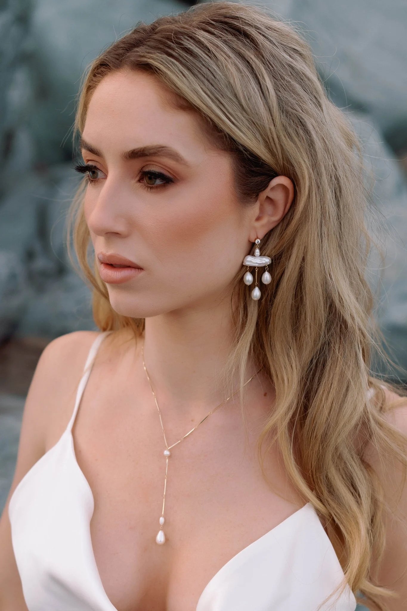 Bride on beach with wedding gown, lariat style drop necklace with pearls & gold-filled freshwater pearl chandelier earrings. Pearl bridal jewelry, pearl jewelry sets, & statement bridal earrings handmade by Canadian bridal designer