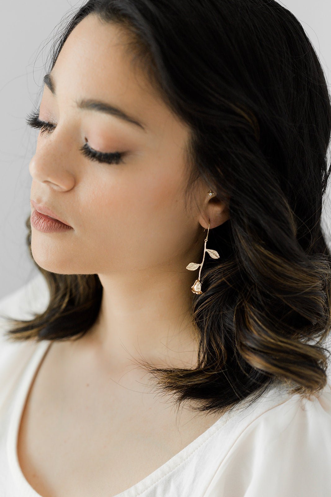 A woman wearing a dangle Orarose Golden Rose Earring; looking wistful. Bridal jewelry Canada. Gold-filled jewelry Canada. Handmade Canadian jewelry. Woman-owned Canadian jewelry brand. Canadian jewelry business.