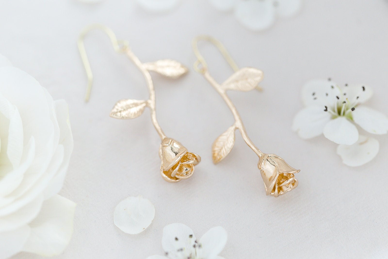 A pair of 14k Gold-filled Orarose Golden Rose Earrings on white background surrounded by white flowers. 