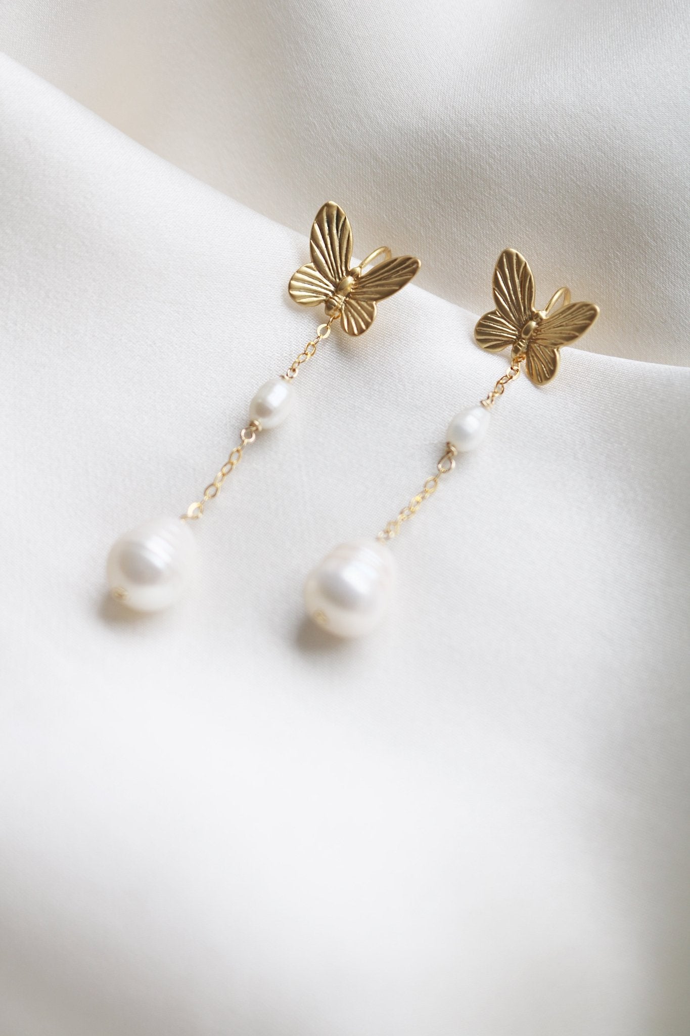 Papillion Earrings in gold-filled with freshwater pearls and butterflies against a white satin sheet. 