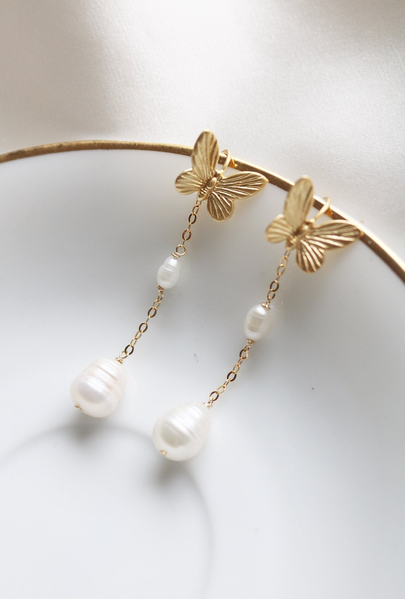 Papillion gold and pearl Earrings displayed on a white plate. 