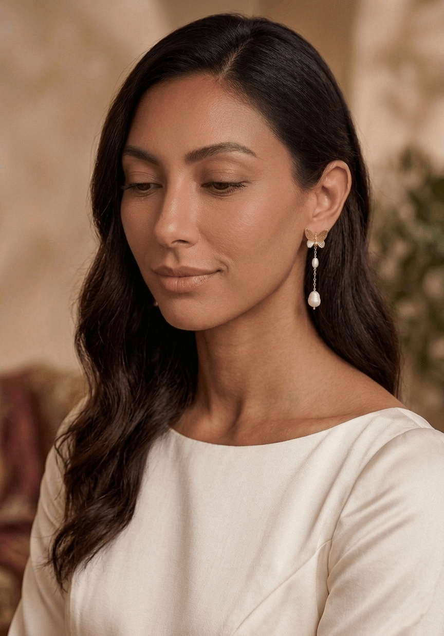 A woman wearing long butterfly earrings with freshwater pearls with long sleeve white satin bridal gown. Pearl Bridal jewelry and Handmade Canadian jewelry by Woman-owned Canadian jewelry business.