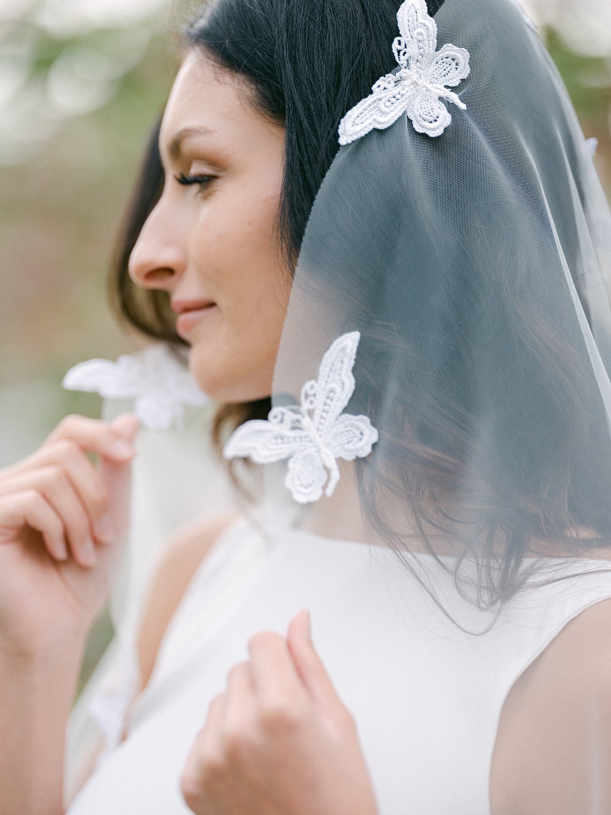 A bride holds her Papillion Lace Butterfly Wedding Veil on either side of her face.