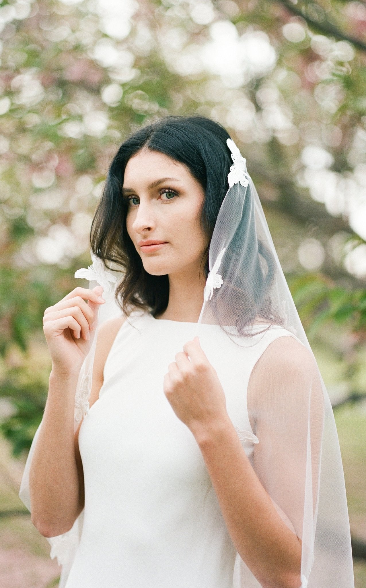 A bride holds her Papillion Lace Butterfly Wedding Veil on either side of her face; looking down the camera. Canadian weddings. Wedding Canada. Wedding veils Canada. Bridal Hair Accessories. Bridal Accessories. Canadian Bridal Accessories. Handmade Canadian Accessories. Canadian handmade Accessories. Canadian designer. Canadian artist.