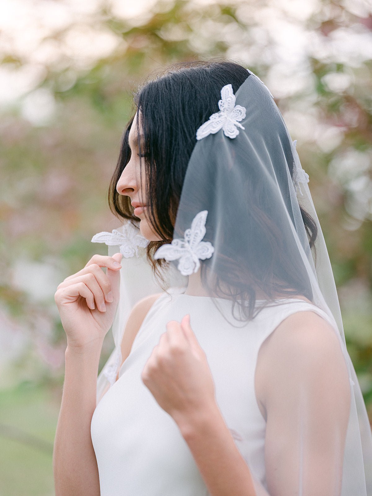 A Lace Butterfly Tulle Wedding Veil being held taut to showcase the lace butterflies with blurred natural background. Canadian bridal veils, handmade wedding veils, & wedding veils Canada