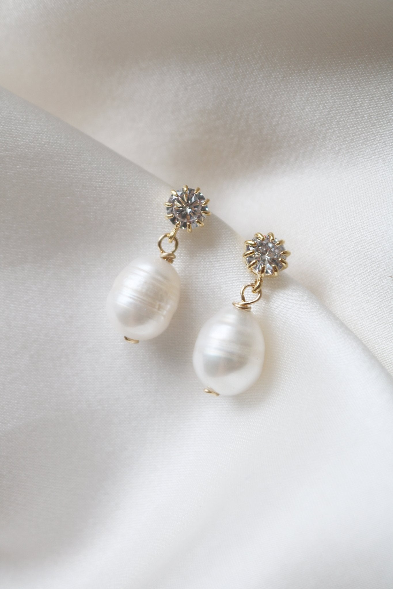 A pair of Party Girl Fresh Water Pearl and Crystal Studs on a white satin sheet. 