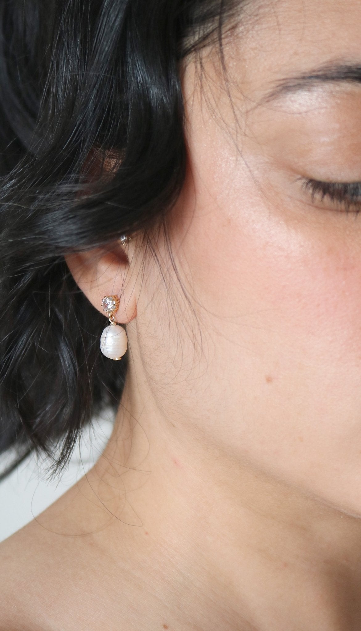 A single freshwater pearl and crystal stud hangs from a woman's ear.