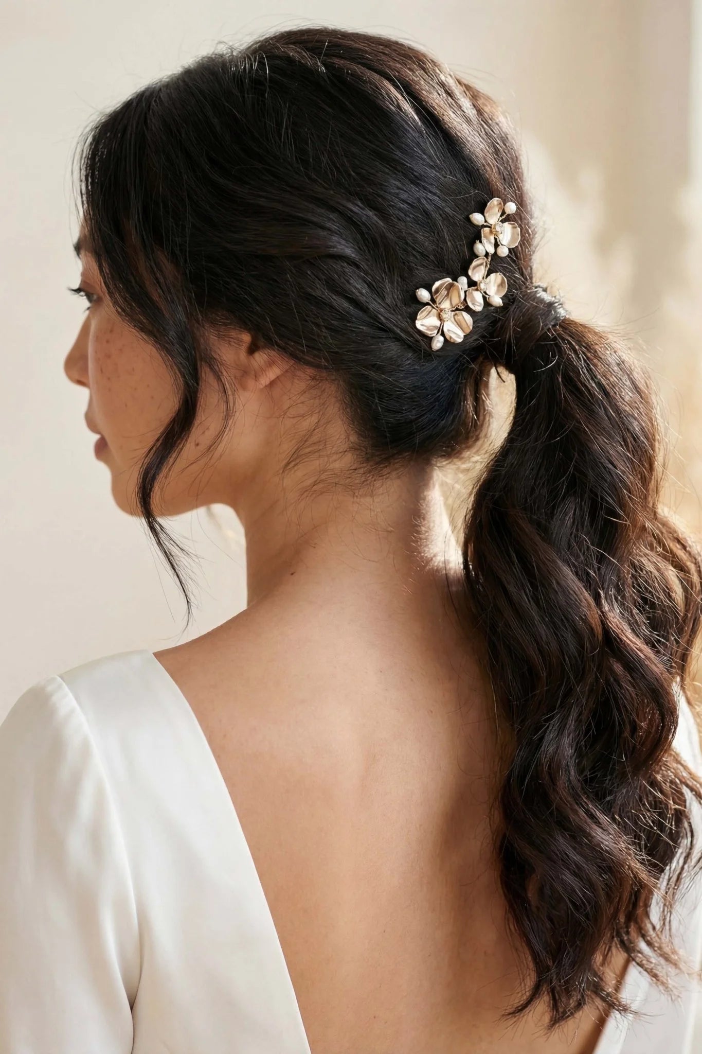 A gold flower bridal hairpin with freshwater pearls and crystals on a Filipina bride with a neutral background. Handmade bridal hair accessories for Canadian weddings. Pearl bridal accessories by small jewelry business.