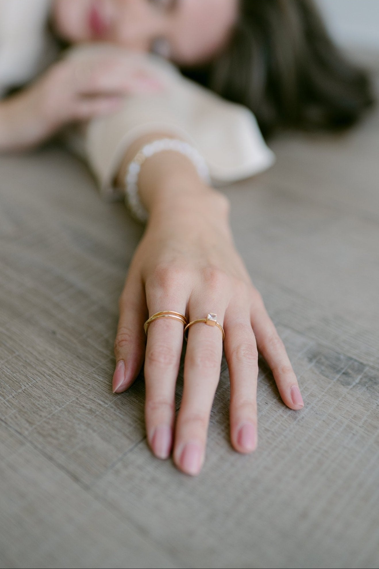 A woman's outstretched arm wearing 2 gold-filled rings against brown surface. Everyday jewelry, modern jewelry designs, & handmade gold-filled jewelry Canada