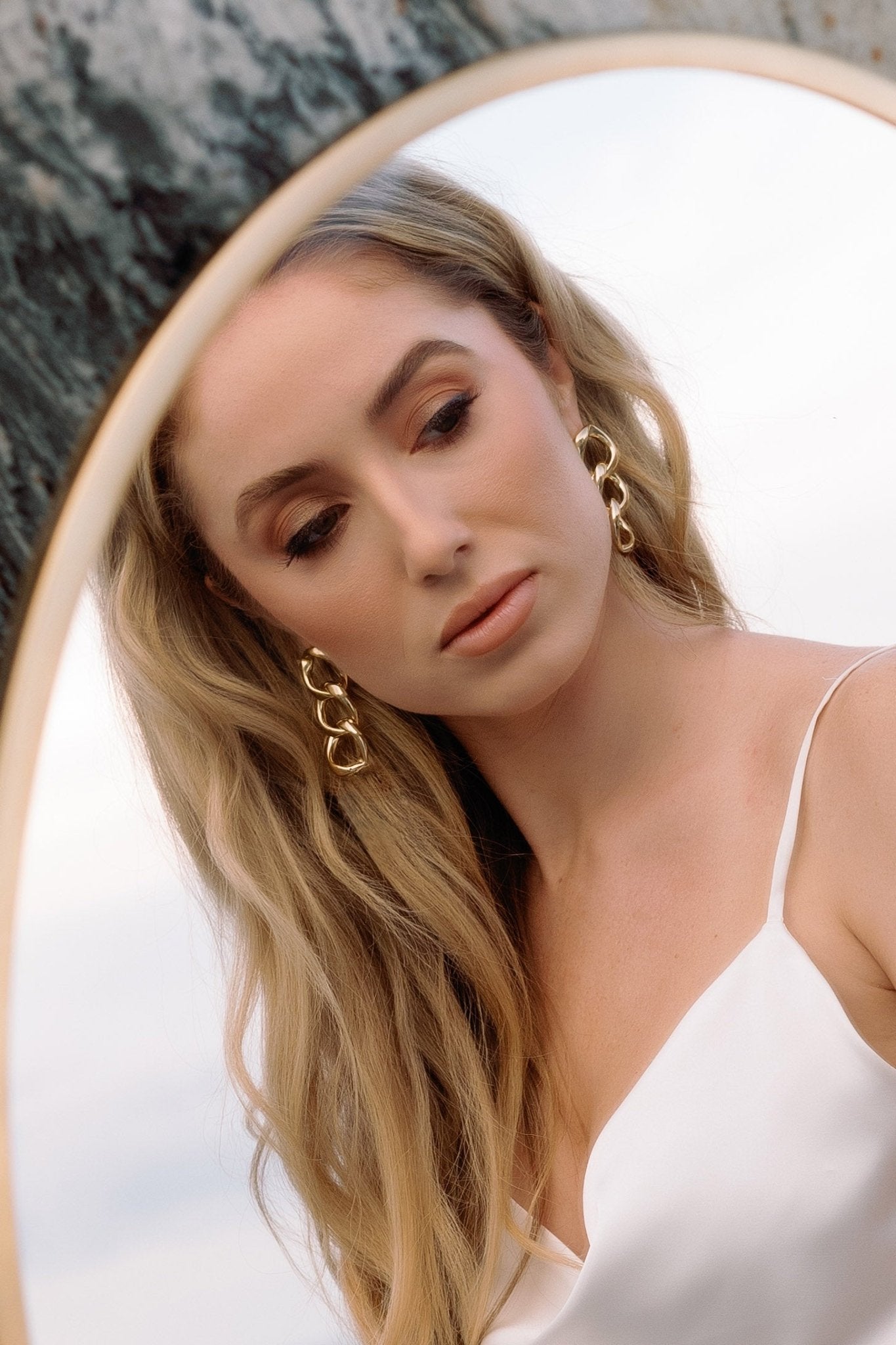 A bride looks at herself in a mirror while wearing a pair of puffy gold-filled chain link earrings.