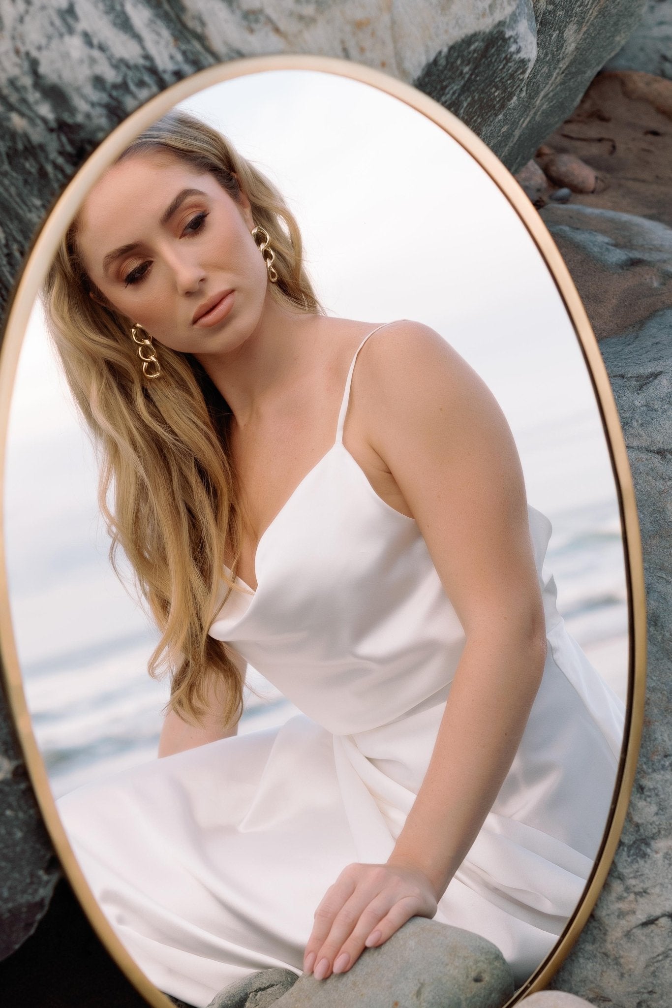 A bride looks at herself in a mirror while wearing a pair of puffy gold-filled chain link earrings.