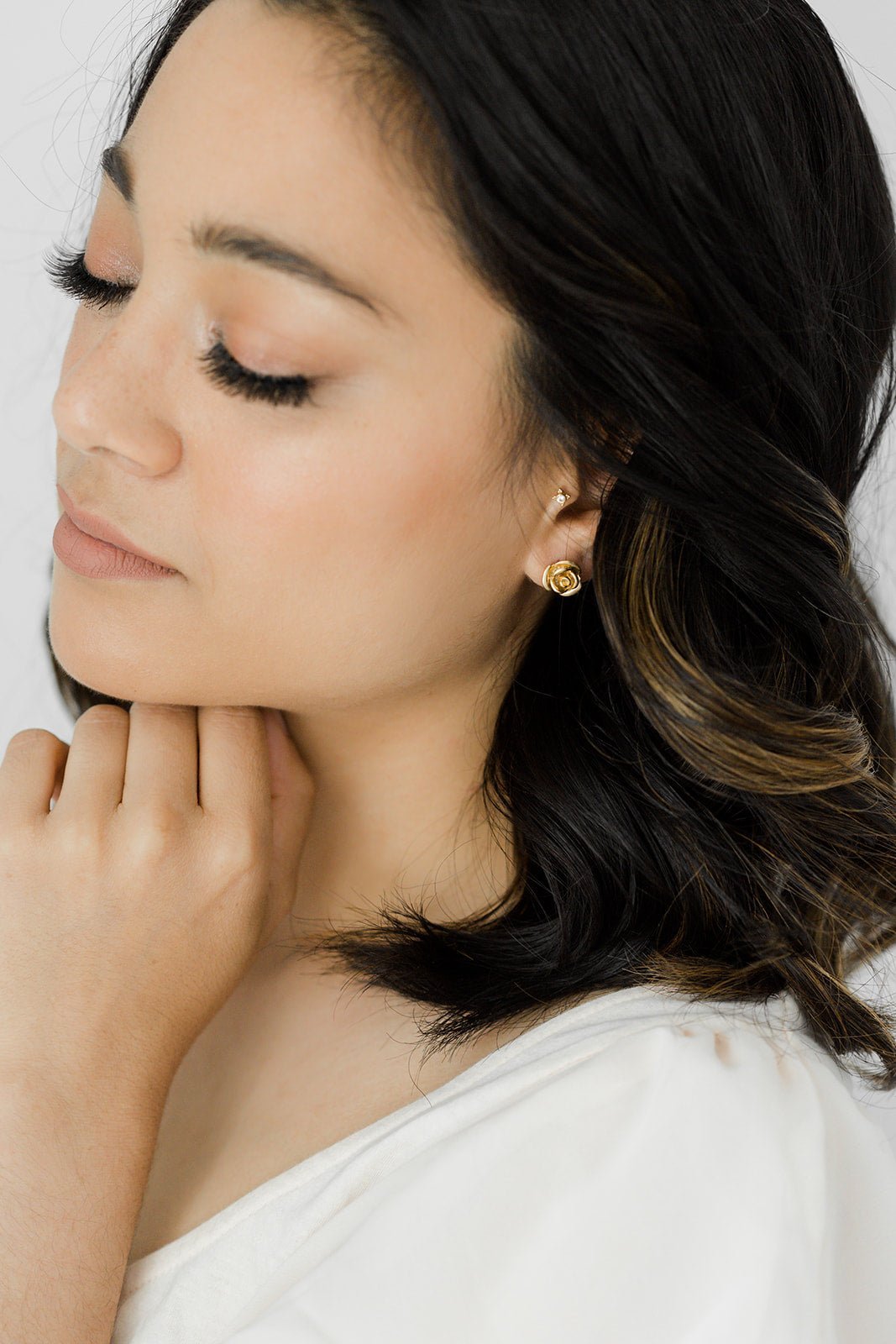 A 14k gold-filled rose stud with sterling silver posts sits on a dark-haired woman's ear. Gold-filled jewelry & handmade Canadian jewelry by BIPOC jewelry designer
