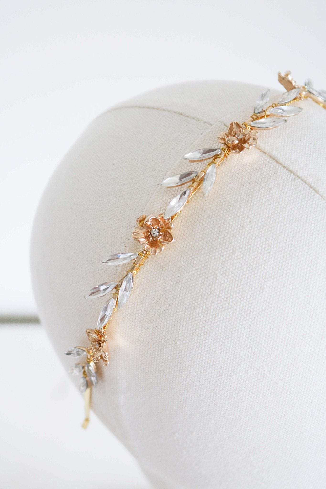 A Gold bridal headband with crystal leaves and gold flowers on a head bust. 