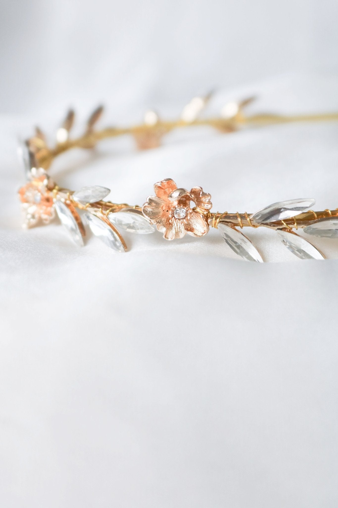 An extreme close-up of the Rosalie Crystal Leaf and Gold Rose Bridal Headband on a white background. 