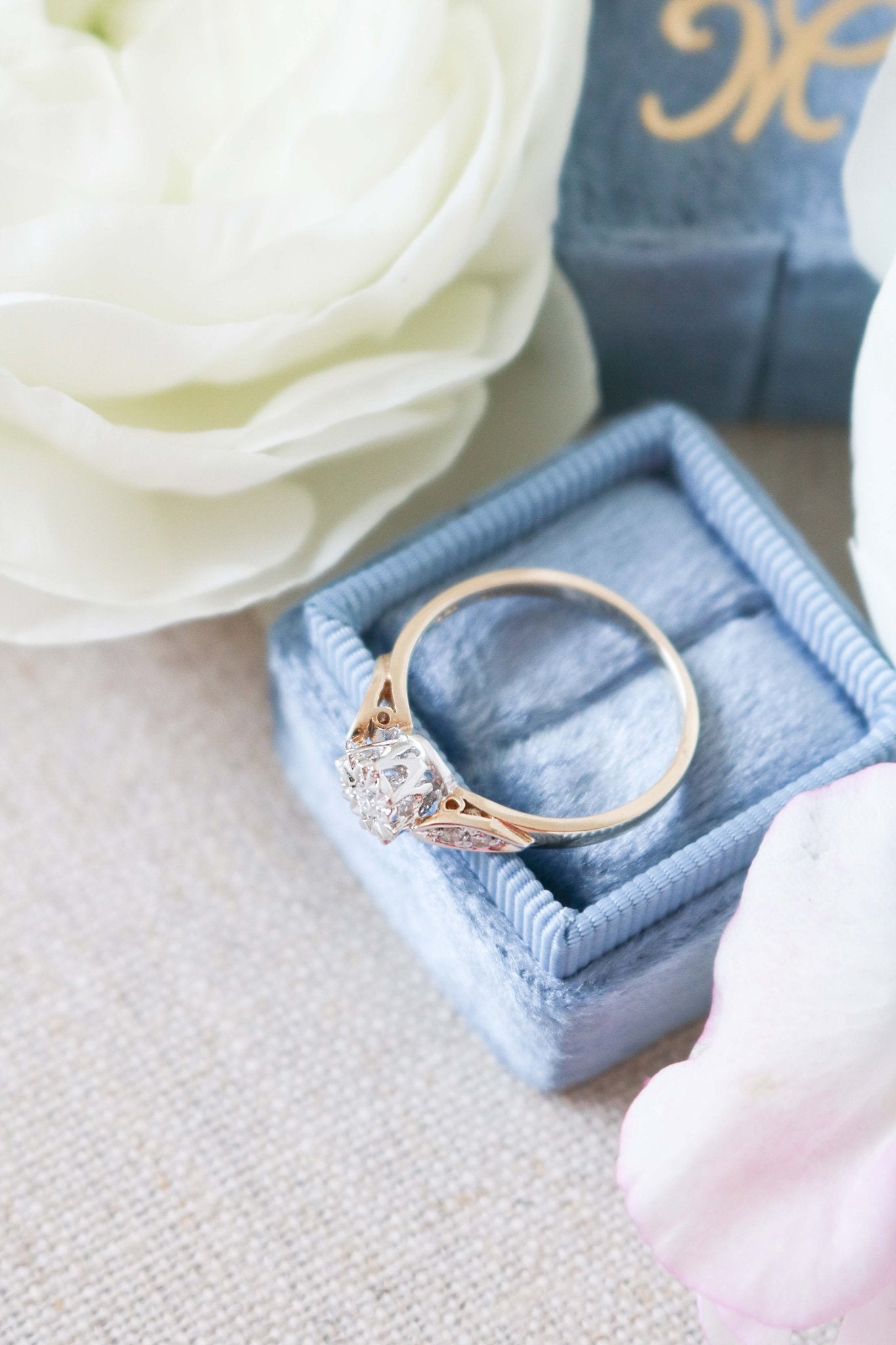 A close up top view of the side of a Serena Diamond Vintage Engagement Ring in 9ct Gold sitting on top of a blue ring box. 