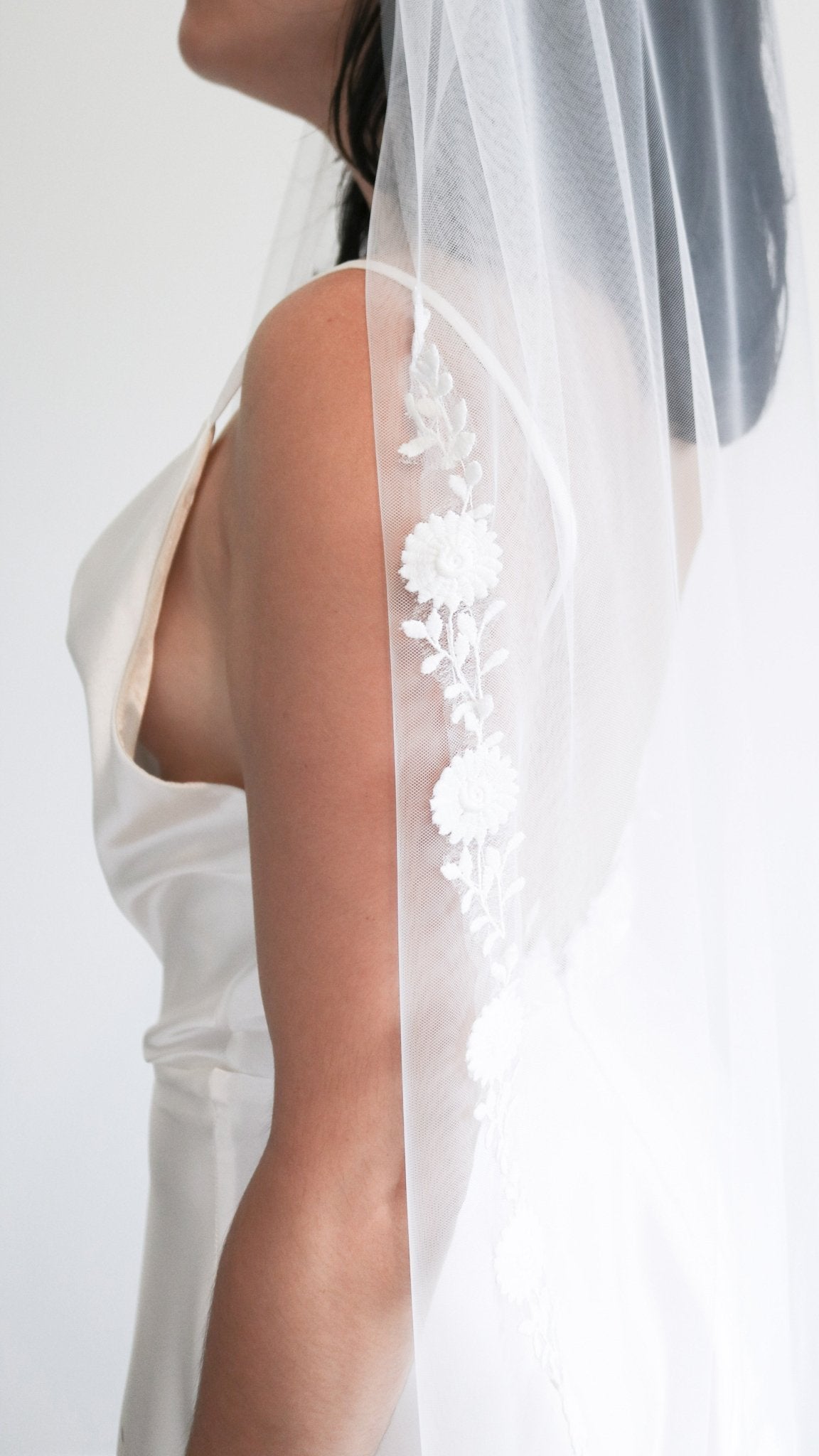 A bride stands tall while her floral vine lace wedding veil trails down her back.