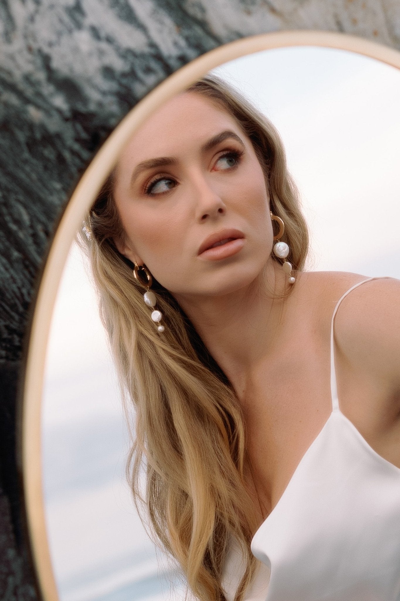 A mirrored bride looks away while showing off her gold-filled freshwater pearl dangle hoops.