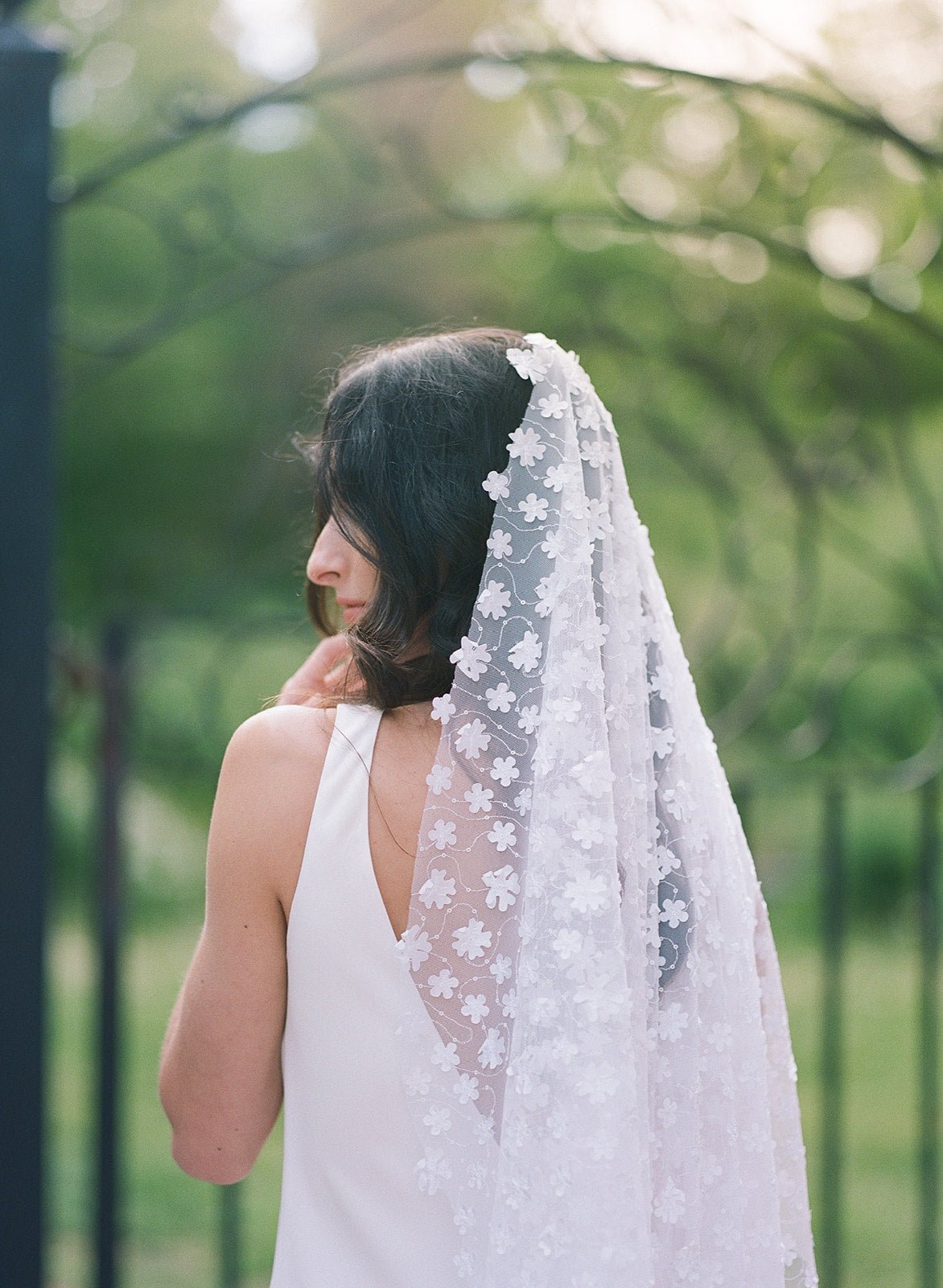 A bride looks coy while her Sonnet floral wedding veil cascades down her back. 