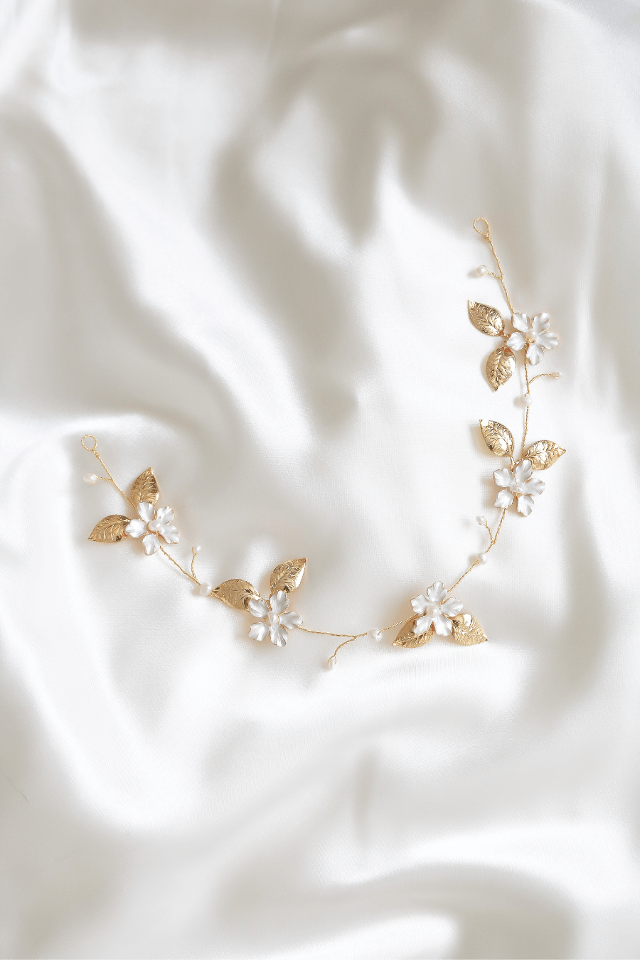 A thin dainty Spring Bridal Hairvine with Fresh Water Pearls lays on a white satin sheet. 