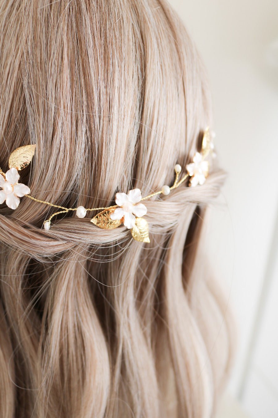 A close up of the wire-wrapped gold bridal hairvine with flowers and freshwater pearls across a bridal braid. 