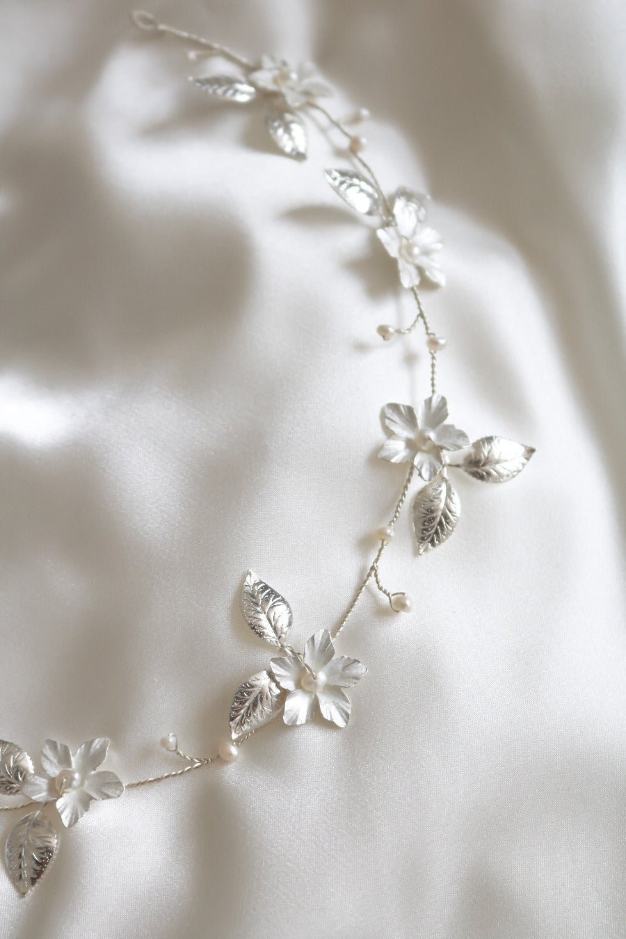 A close up of the Spring Bridal Hairvine with Fresh Water Pearls in Silver on a white satin sheet. 