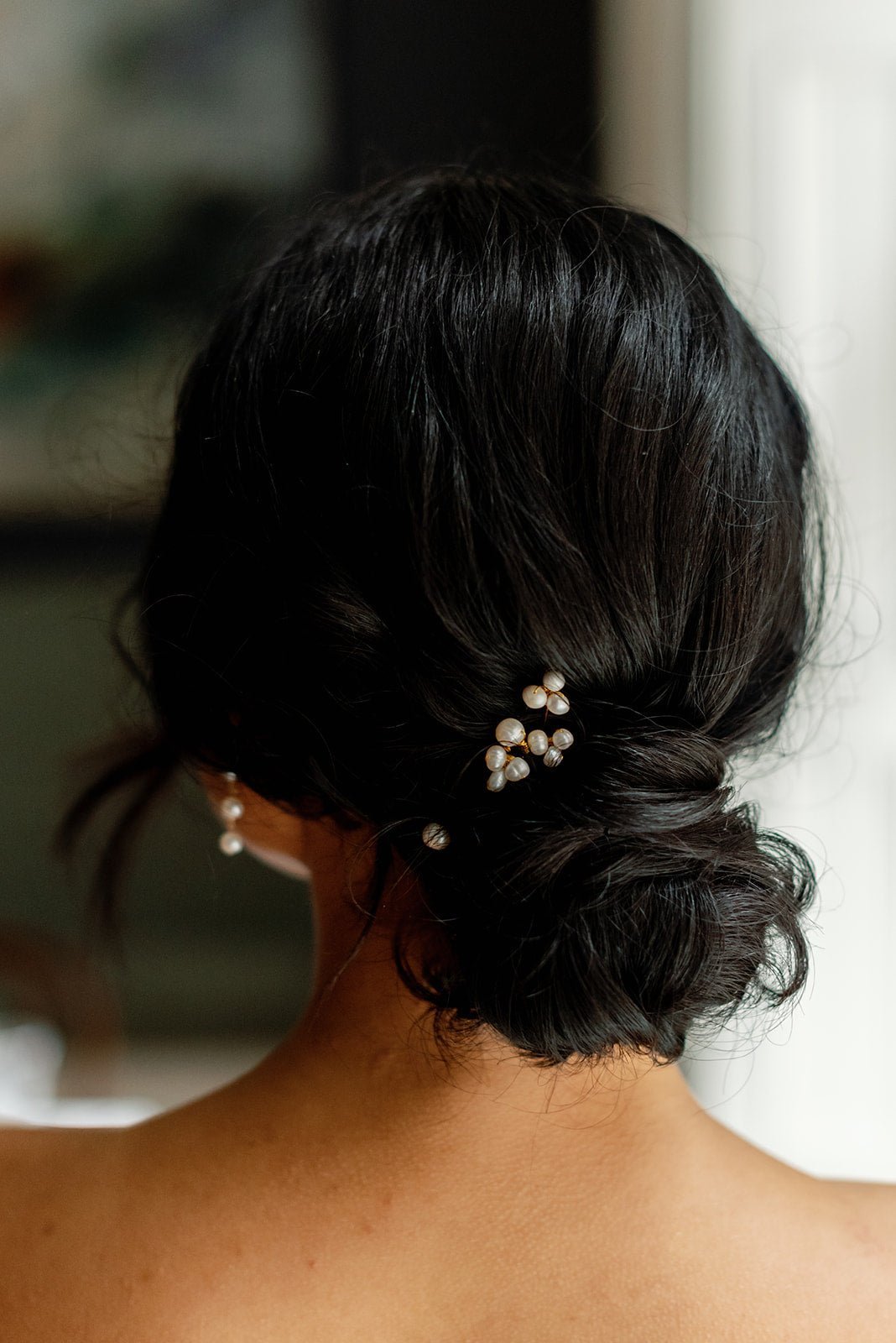 A cluster of gold freshwater pearl bridal hairpins set in a dark-haired bridal up-do bun with blurred background. Bridal hair accessories, handmade bridal accessories, & handmade hair accessories Canada