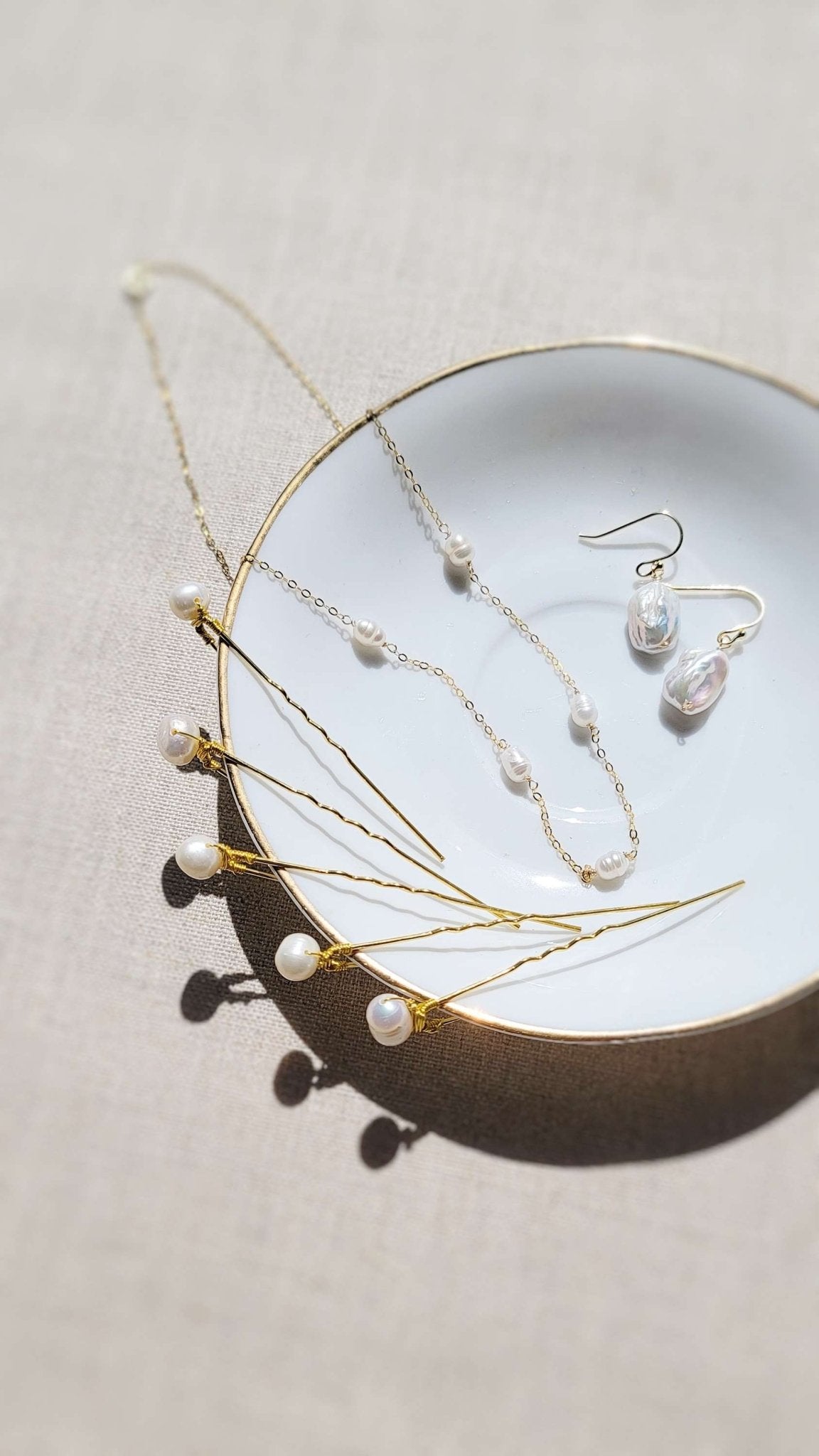 Several gold freshwater pearl bridal hairpins on a dish with gold-filled freshwater pearl earrings and necklace. 