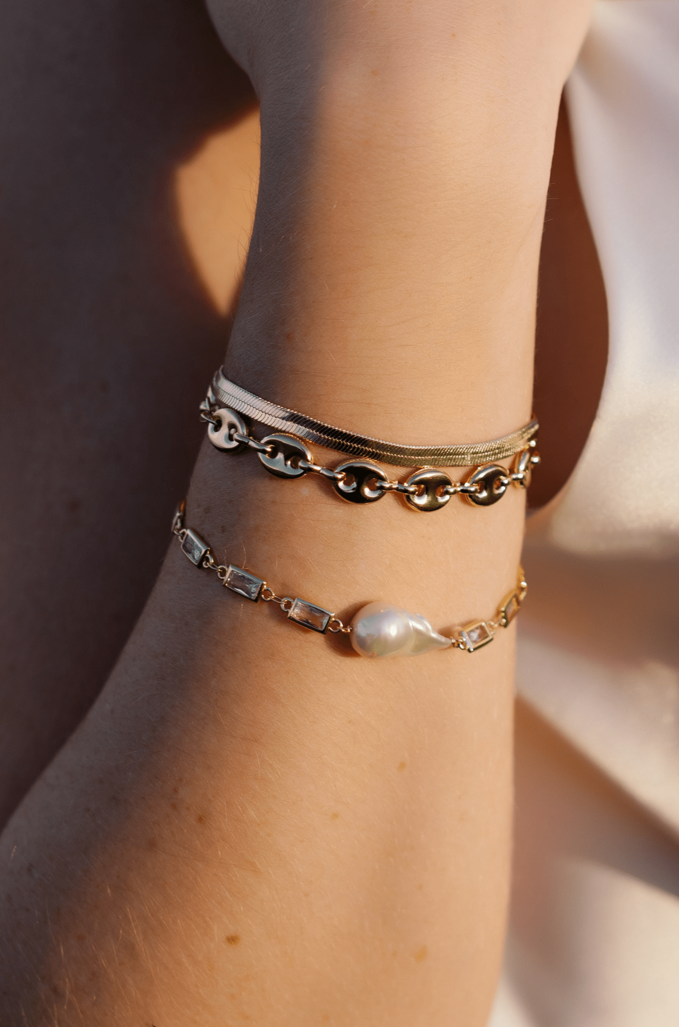 Gold-filled bracelet stack with herringbone chain, puffy mariner link, and crystal link bracelet with baroque pearl. 