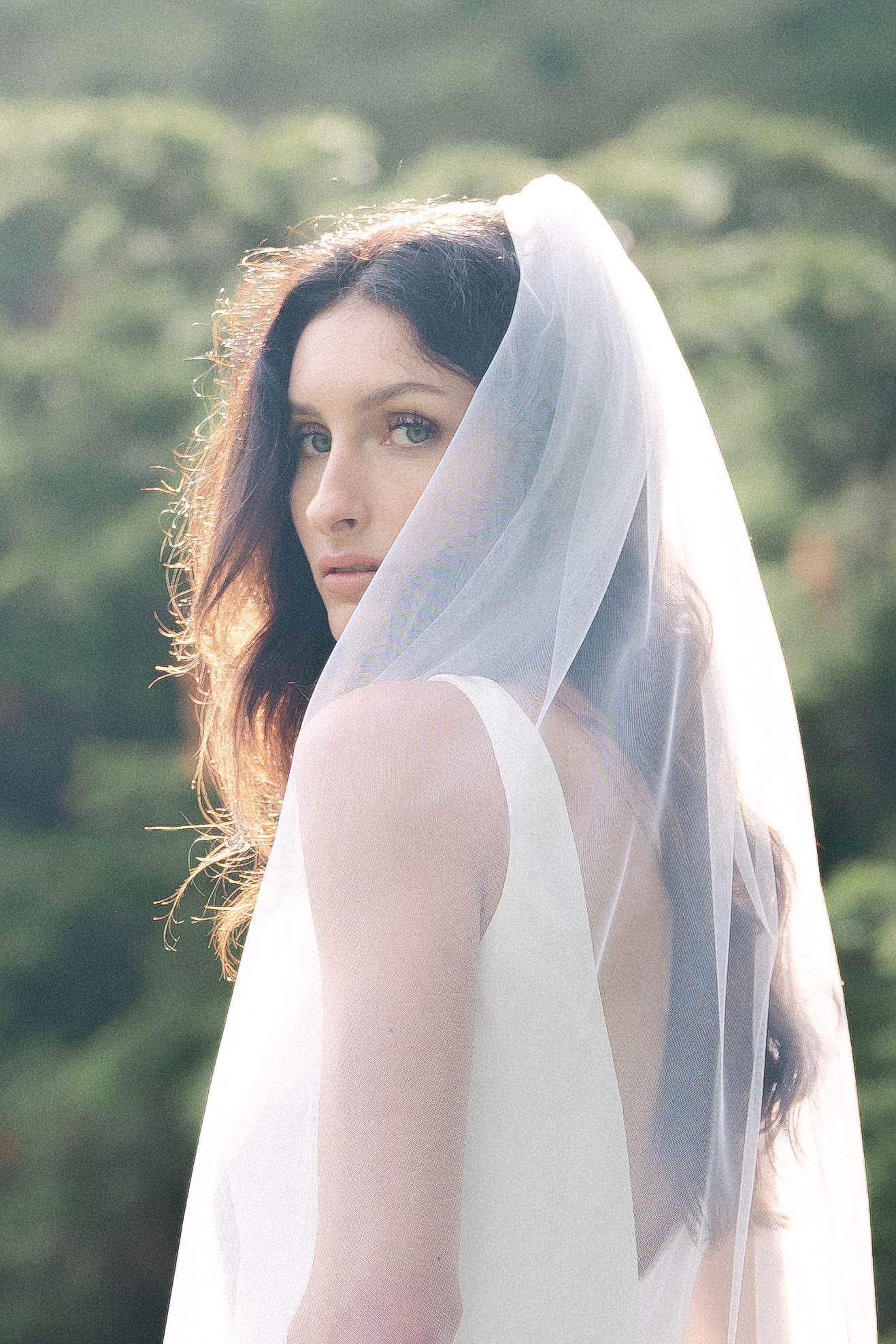 A close up of the Beloved Traditional Tulle Wedding Veil draped over a bride as she looks over her shoulder. 