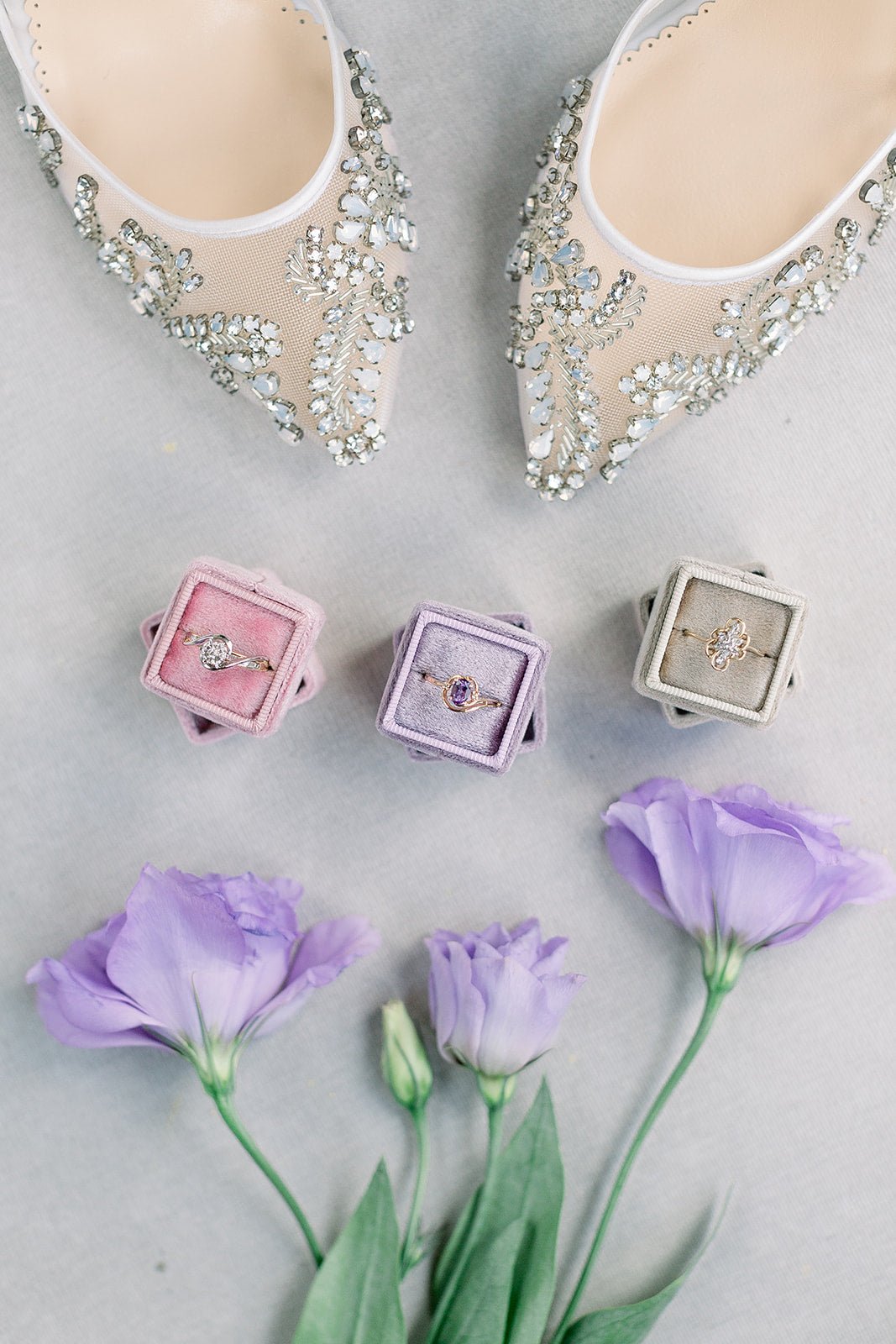 A line of three vintage engagement rings in ring boxes with purple flowers and crystal bridal shoes. 