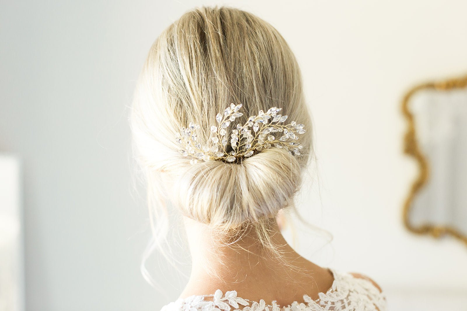 A gold crystal bridal hair comb tucked into a tight blonde bridal bun with blurred background. Bridal Hair Accessories, Canadian Bridal Accessories, & handmade Canadian accessories by BIPOC bridal designer