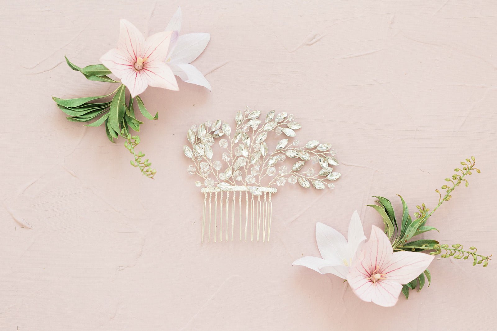 A silver Crystal leaf Bridal Hair Comb and flowers on pale pink surface. Bridal Hair Accessories,  Canadian Bridal Accessories, & Handmade Canadian Accessories by BIPOC bridal designer