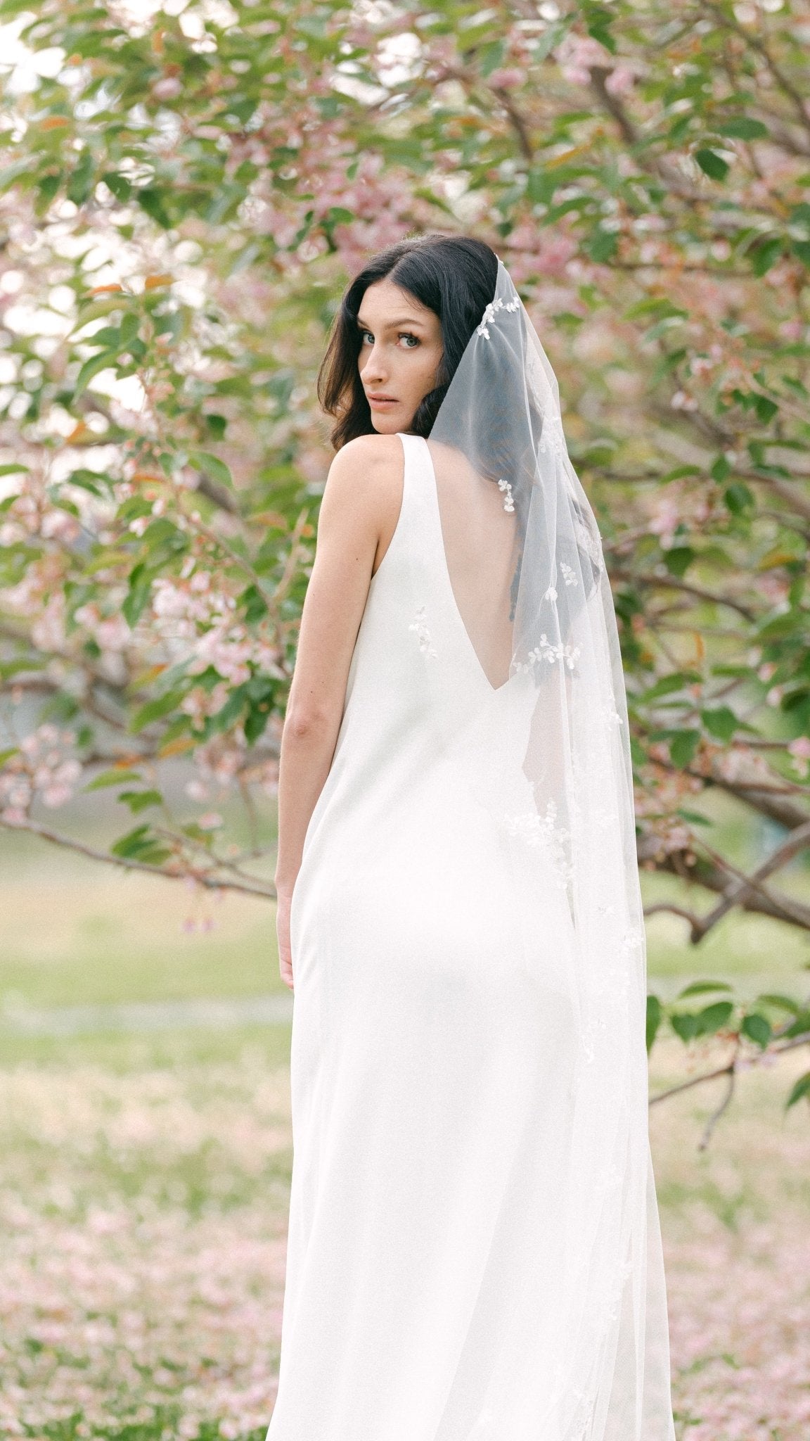 A bride in a white wedding dress looks over her shoulder; her Wisteria lace leaf wedding veil trailing behind her. Canadian weddings. Wedding Canada. Wedding veils Canada. Bridal Hair Accessories. Bridal Accessories. Canadian Bridal Accessories. Handmade Canadian Accessories. Canadian handmade Accessories. Canadian designer. Canadian artist.