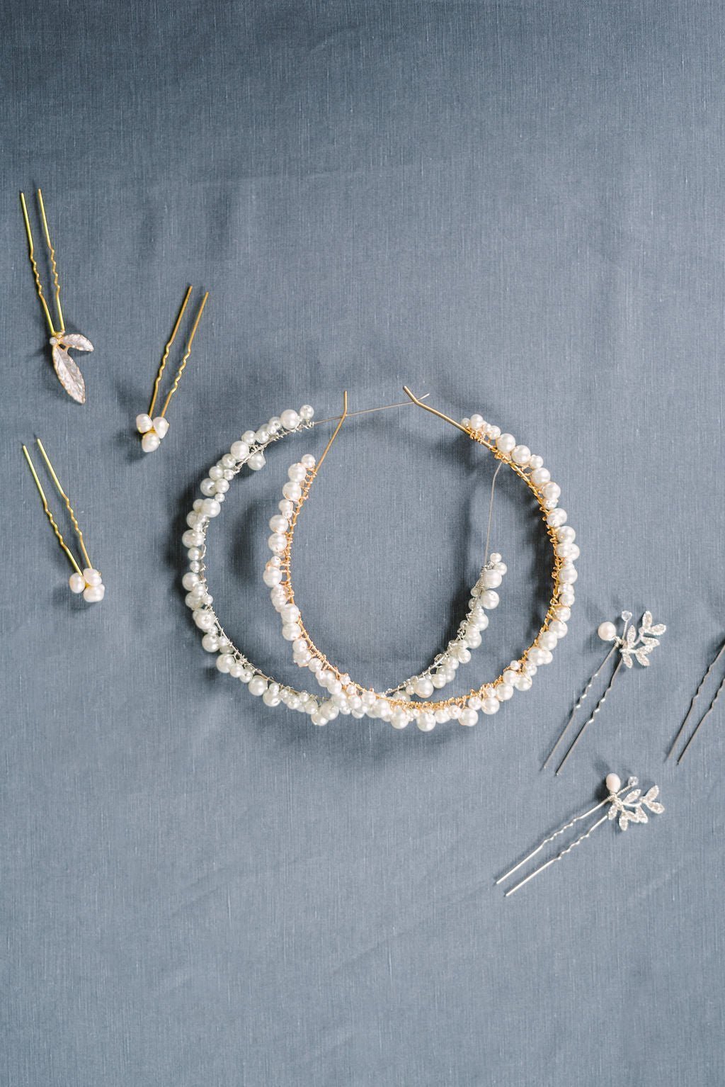 Two Swarovski pearl headbands in gold & silver surrounded by wedding hairpins on pale blue fabric surface. Canadian Bridal Accessories & Handmade Canadian Accessories by BIPOC wedding designer